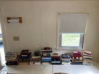 Wide shot of all book stacks on table under window showing quantity and condition.