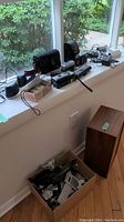 Windowsill display of two black AmazonBasics Bluetooth speakers, black camera cases, film cameras, cables and remotes