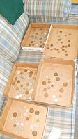 Overview of multiple cardboard trays containing various international coins scattered inside them placed on a plaid couch.