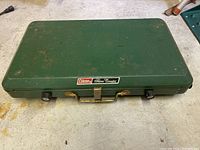 Closed view of green Coleman camp stove case with handle and front control knobs.
