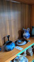 Shelf with two blue and black vases, a matching blue and black bowl, blue and white decorative pitcher, and a darker glazed pitcher.
