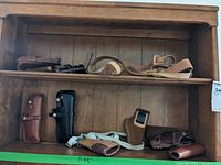 Various holsters on wooden shelves showing multiple leather holsters in different colors and styles.