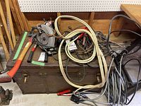 Assorted tools, jumper cables, and hand tools on wooden surface over a metal trunk.