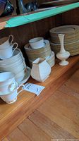 Shelved items: stacks of Oxford bone china plates, cups, saucers, and two white vases