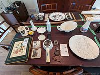 Wide shot showing entire lot on wood dining table including ceramic vases and bowls, plates, coasters, magnifying glasses, doilies and placemats.