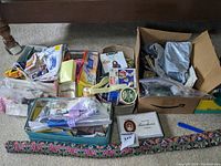 Photo showing multiple boxes filled with assorted sewing notions and supplies including buttons, zippers, thread, and fabric scraps.