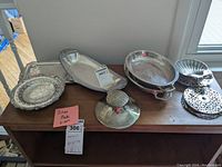 Full view of all silverplated serving trays and platters displayed on a wooden table near a window.