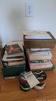 Photo showing stacks of several boxes filled with loose and boxed greeting cards on a wooden floor.