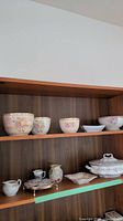 Shelf with porcelain bowls featuring floral designs and other matching porcelain pieces including pitchers and a tureen.