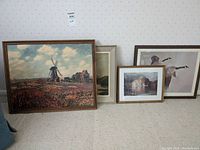 Five framed prints leaning against a wall with a mix of scenic and geese wildlife themes, varied sizes and frames.
