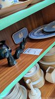 Shelf containing blue and white Wedgwood plates, a small blue Wedgwood plaque or miniature tray, and a dark multi-piece Nessie figure with several segments, with white plates stacked below.