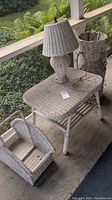 Weathered wicker side table with woven wicker lamp on top and a wicker vase and magazine rack on the side.