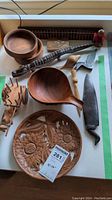Top view of wooden decor items including bowls, wooden knife, spoon, carved plate, puzzle toy, and figurine arranged on a white surface