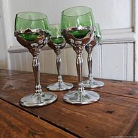 Four mid-20th century aperitif glasses with green glass bulbs clipped into chrome stems on a wood surface.