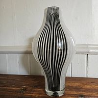 Full view of the tall Murano glass vase with black vertical stripes against a wall.