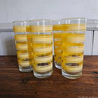 Four vintage glasses arranged in a group showing overall design and style with yellow stripes and clear glass.