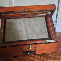 Open wooden case showing the printing board covered with fabric mesh and hinged frame inside