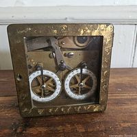 Front view showing brass casing with dual numbered white dials and visible internal gears behind glass.