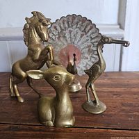 Four brass animal figurines displayed on wooden surface: rearing unicorn, painted peacock with tail, long-legged bird, and sitting fawn.