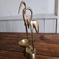 Side view of brass incense burner showcasing the two stylized cranes with red gemstone eyes and the incense bowl on a wooden surface.