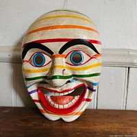 Front view of the wooden mask with colorful horizontal stripes and painted facial features.