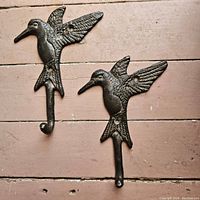 Pair of cast-iron coat holders shaped like hummingbirds mounted on a wooden floor showing size and detail