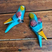 Full view of the pair of ceramic birds on a wooden surface showing the overall size, color and hanging holes
