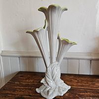 Full view of the white floral vase shaped with three trumpet-like flower openings and leaf base, standing on wooden surface.