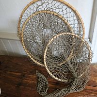 Full view of three-ring fishing net leaning against wall showing all rings and netting in natural wood and brown net materials.