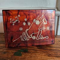 Top view of the rectangular amber plastic jewelry box with gold detailing including floral and bracelet motif and text.