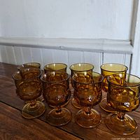 Group of eight vintage amber goblets arranged in two rows on a wooden surface, showing uniformity and condition.