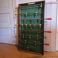 Foosball table standing vertically showing entire table, players on rods, and the wood frame.