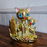 Front angle view of the gold cat bank showing two cats, one larger and one smaller, with painted flowers at base.