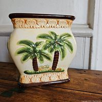 Front view of the square ceramic planter showing the palm tree motifs and decorative patterns along the rim and base.