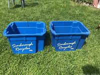 Two blue rectangular recycling bins with 'Scarborough Recycles' printed on the front, placed on grass outdoors.
