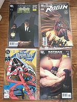 Four Batman comics laid out on wood surface showing front covers: two Batman Legends of the Dark Knight comics, one Robin comic book, one Batman Detective Comics comic.