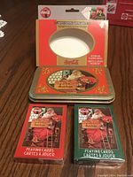Front view of metal Coca Cola souvenir tin with holiday Santa Claus design, shown with two unopened playing card packs in red and green boxes.
