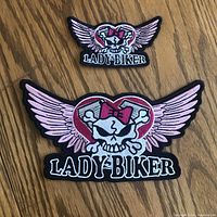 Two embroidered lady biker patches, one large and one small, on wooden surface.