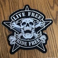 Large embroidered biker patch showing skull with crossed bones and star, with 'Live Free Ride Free' text, laid flat on wooden floor.