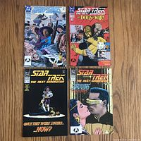 Four Star Trek The Next Generation comics laid flat on a wooden surface, showing colorful cover art and titles.