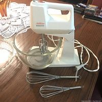 Sunbeam Mixmaster stand mixer with glass bowl and two whisks on wooden table.