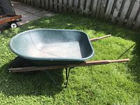 Side view of the green Garant wheelbarrow on grass, showing plastic basin and wooden handles.