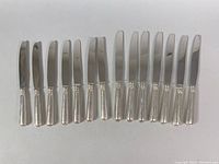 14 knives laid out horizontally showing polished blades and sterling silver handles