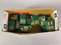Photo of the multiple original boxed Goebel bisque angel bell ornaments inside a larger box, viewed from top, showing green boxes each labeled with a year
