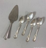 Photo showing four sterling silver spoons and one cheese cutter with decorated handles.