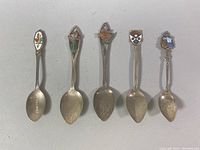 Photo of all five sterling silver collector's spoons laid side by side showing enamel decorated heads and varying handle styles.