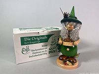 Front view of the Erzgebirge German smoking woman gnome incense burner with original box behind.