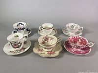 Photo showing five different teacup and saucer sets arranged in two rows with various floral and leaf designs.