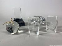Five crystal and glass paperweights including diamond cut, animal engravings and glass apple with gold stem.
