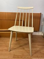 Front angle view of the chair showing the spindle backrest, tapered legs, and painted finish with signs of wear.